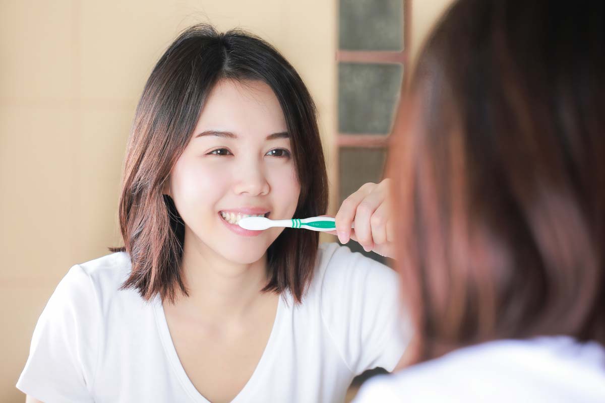 woman brushing her teeth knowing the Causes of Receding Gums