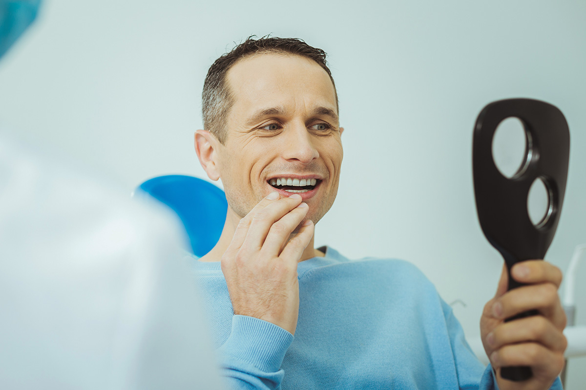 Types of Dentures a man holds up a mirror as he considers types of dentures and dental implants